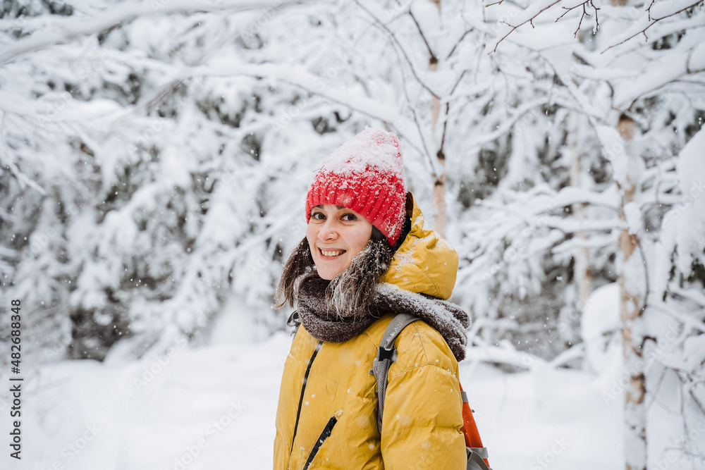 A girl on the street smiles beautifully in winter. A young woman walks in the park in the cold season, snow falls, a beautiful winter forest. The girl laughs, looks straight.