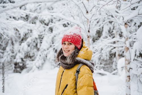A girl on the street smiles beautifully in winter. A young woman walks in the park in the cold season, snow falls, a beautiful winter forest. The girl laughs, looks straight. © Aleksey