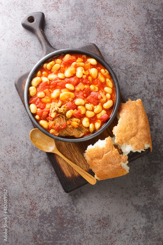 Loubia is a Moroccan dish it is a white bean stew made with tomatoes, garlic, spices like cumin closeup in the bowl on the wooden board. Vertical top view from above photo