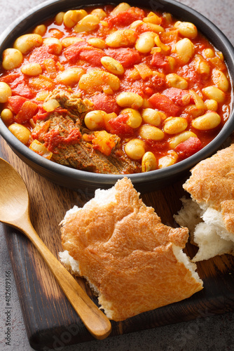 Loubia is a Moroccan dish it is a white bean stew made with tomatoes, garlic, spices like cumin closeup in the bowl on the wooden board. Vertical photo