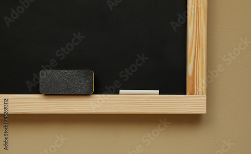 Obraz na płótnie Clean blackboard with chalk and duster hanging on beige wall