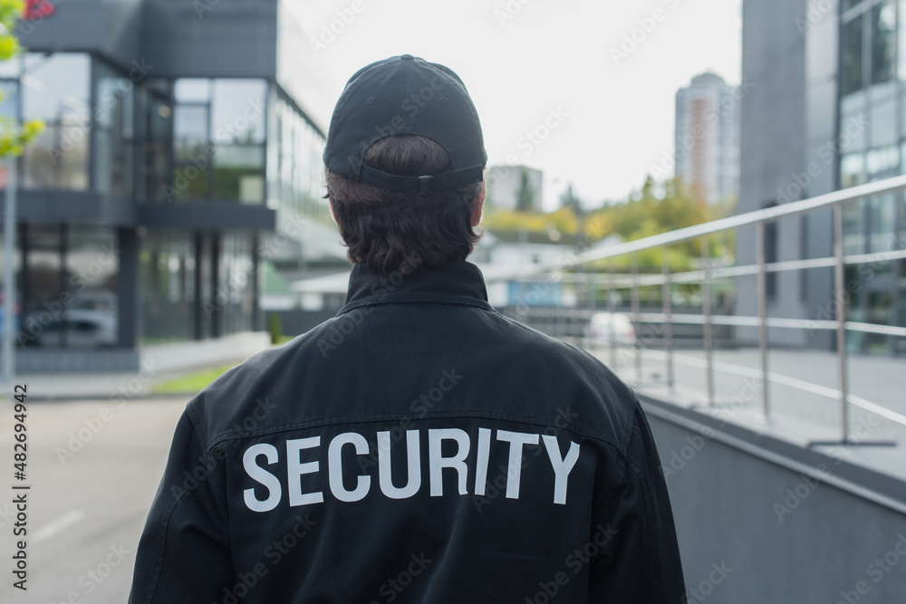 back view of guard in uniform with security lettering standing on city street. back view of guard in uniform with security lettering standing on city street.