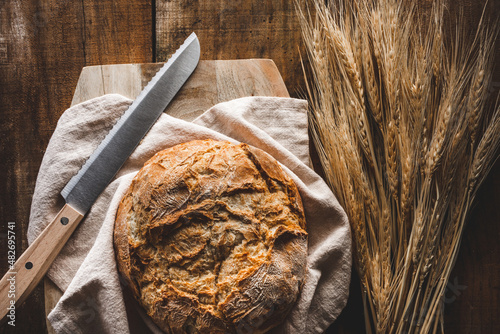 vista superior de una hogaza de pan con un cuchillo sobre una tabla de cortar, con espigas de trigo, en una mesa de madera rústica photo