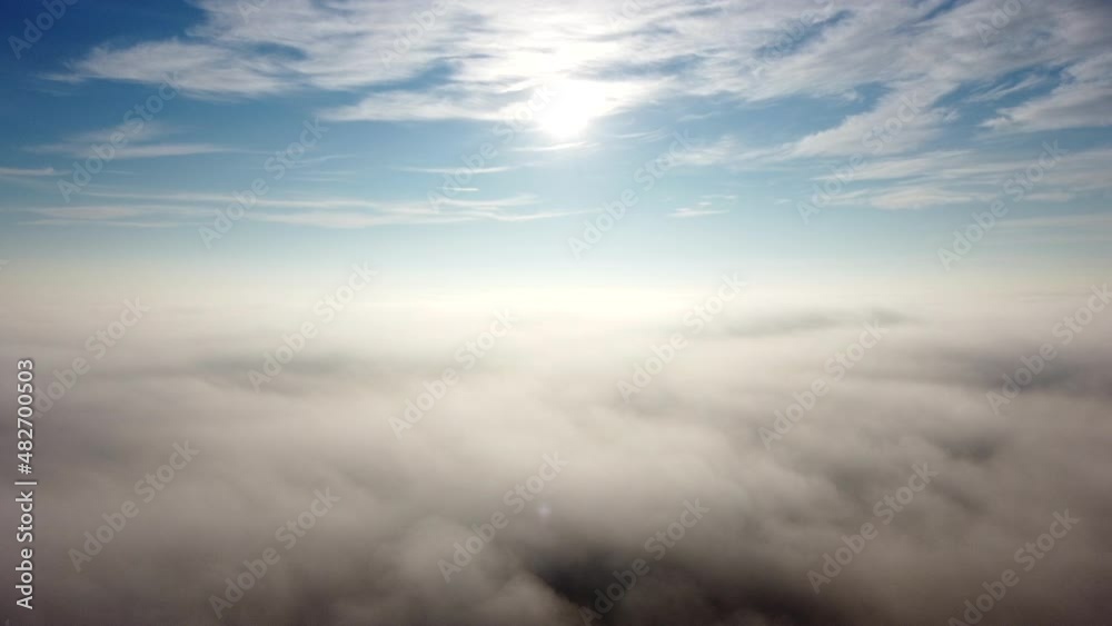 Aerial drone view flight over fog and under clouds with shining sun shining. Fly through clouds. Amazing beautiful nature landscape. Scenic aerial view moving white clouds in blue sky. Seamless loop.