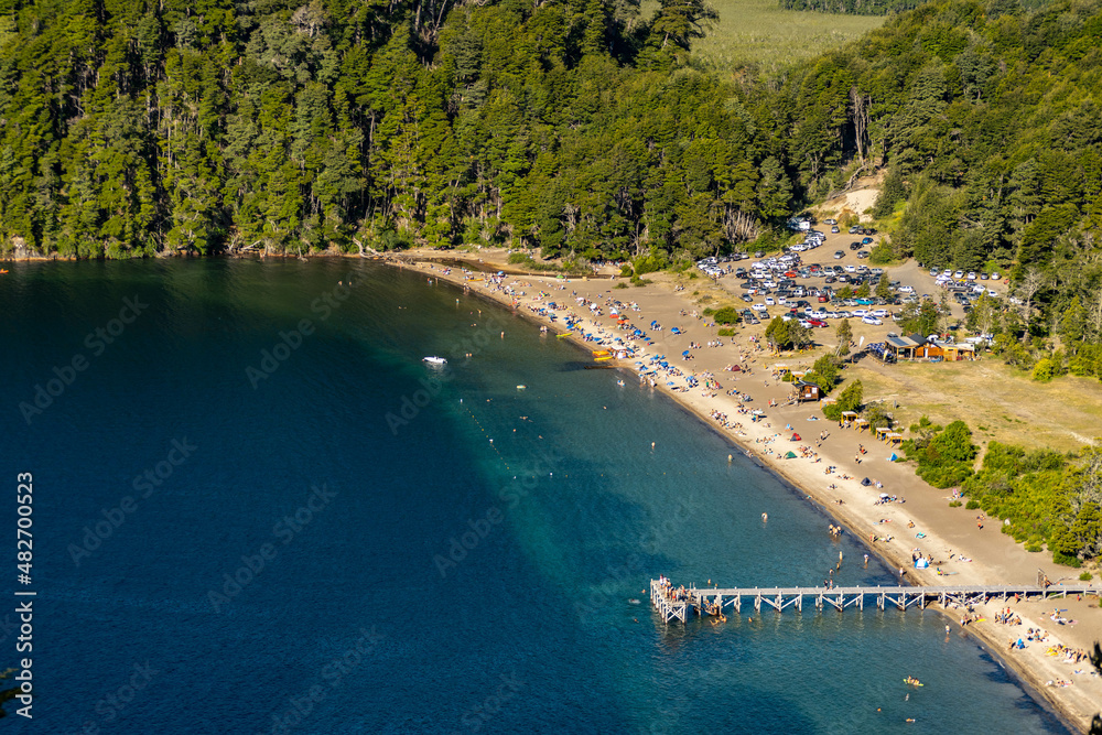 playa lago de agua color azul y celeste con arboles y montaña . personas disfrutando del verano