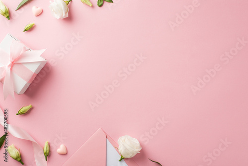 Top view photo of woman's day composition giftbox with bow pink ribbon envelope with card hearts and prairie gentian flowers on isolated pastel pink background with blank space