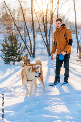Young man with Akita Inu dog in park. Snowy winter background. Sunny day. The concept of friendship between a man and a dog.