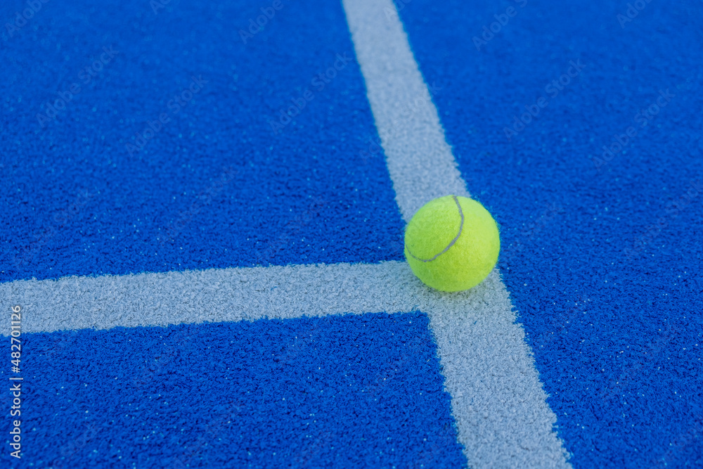 A ball on the line of a paddle tennis court of blue synthetic grass.