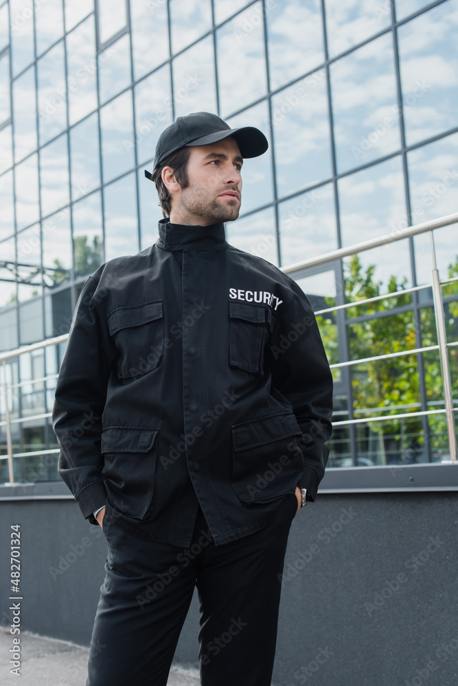 young security man standing with hands in pockets of black uniform and looking away outdoors. young security man standing with hands in pockets of black uniform and looking away outdoors.