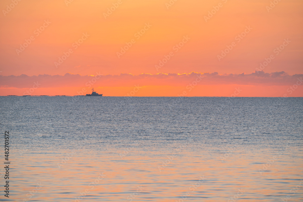 Calm sea at sunrise with fishing boat in distance Calm sea at sunrise with fishing boat in distance