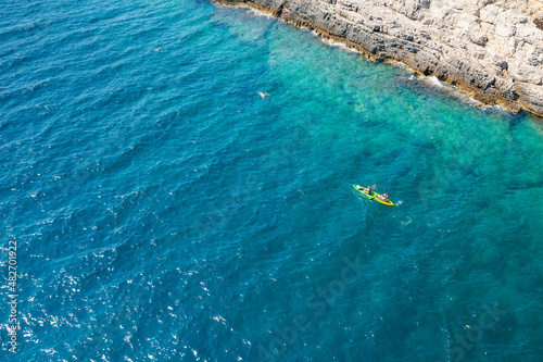 Top view of sportsmen or tourists kayaking in the turquoise transparent blue water of Adriatic sea rocky shore. Summer leisure activity in the canoe. 