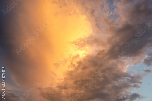 Dramatic sky at sunset with puffy clouds lit by orange setting sun.