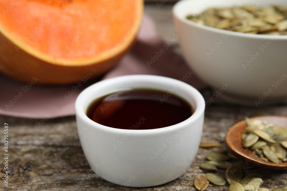 Bowl of pumpkin oil and seeds on wooden table, closeup Bowl of pumpkin oil and seeds on wooden table, closeup