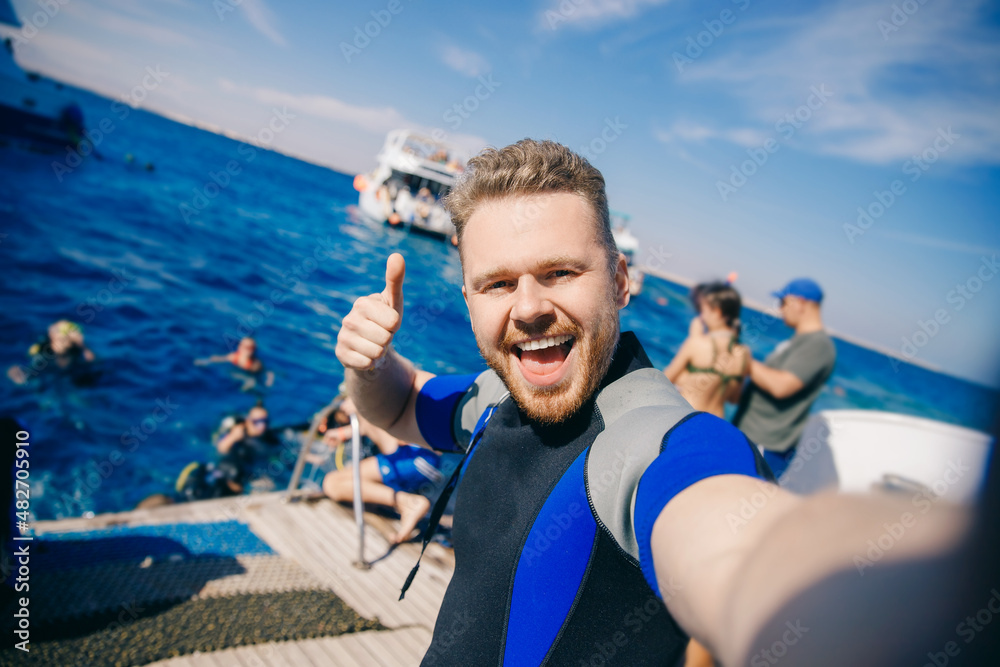 Selfie happy tourist man diver in wetsuit is preparing to dive into sea on boat. Concept diving trip Egypt