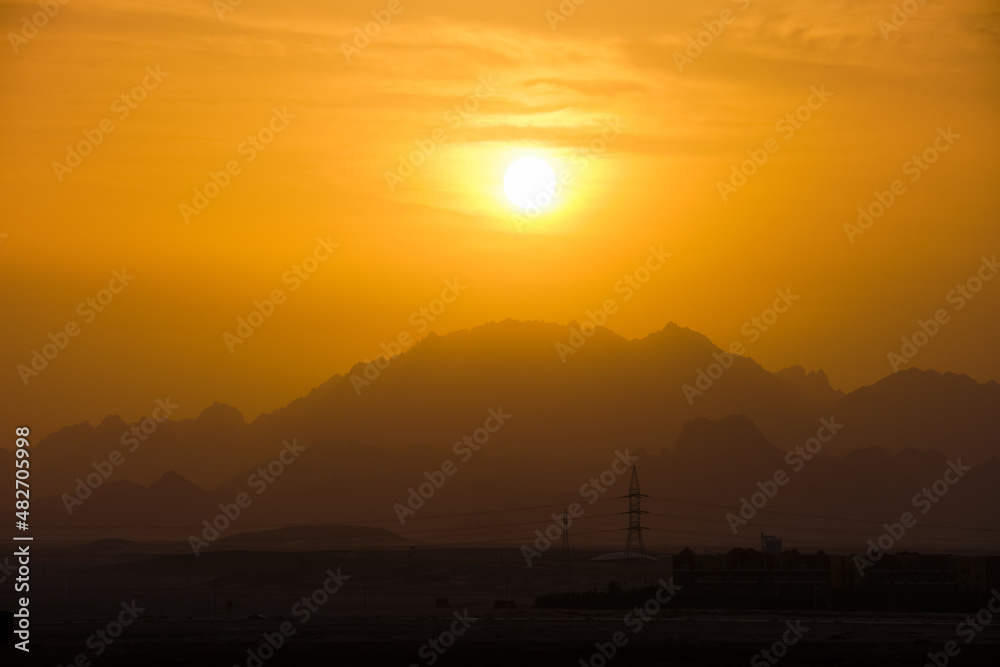 Beautiful evening panoramic landscape with bright setting sun over distant mountain peaks at sunset