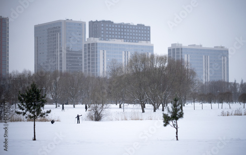 People are skiing and walking in the snow in the city park. Winter holidays in the city. Architecture in winter.