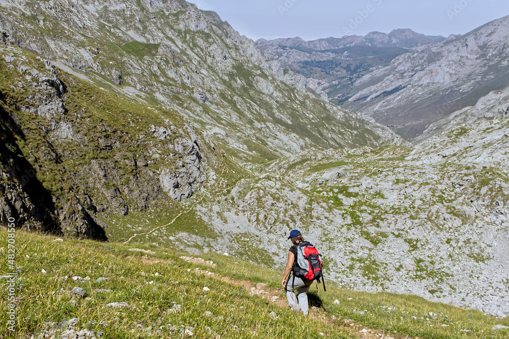 woman with backpack descending through a valley between mountains