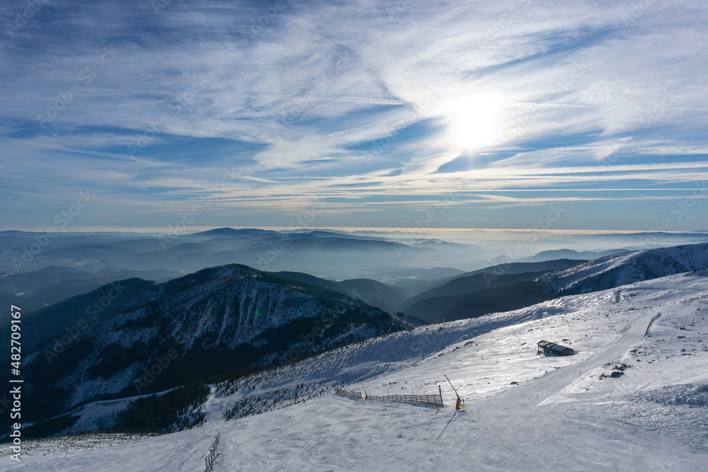 Obraz premium Valley of hilghland mountain winter resort on bright sunny day. Panoramic wide view of downhill slopes