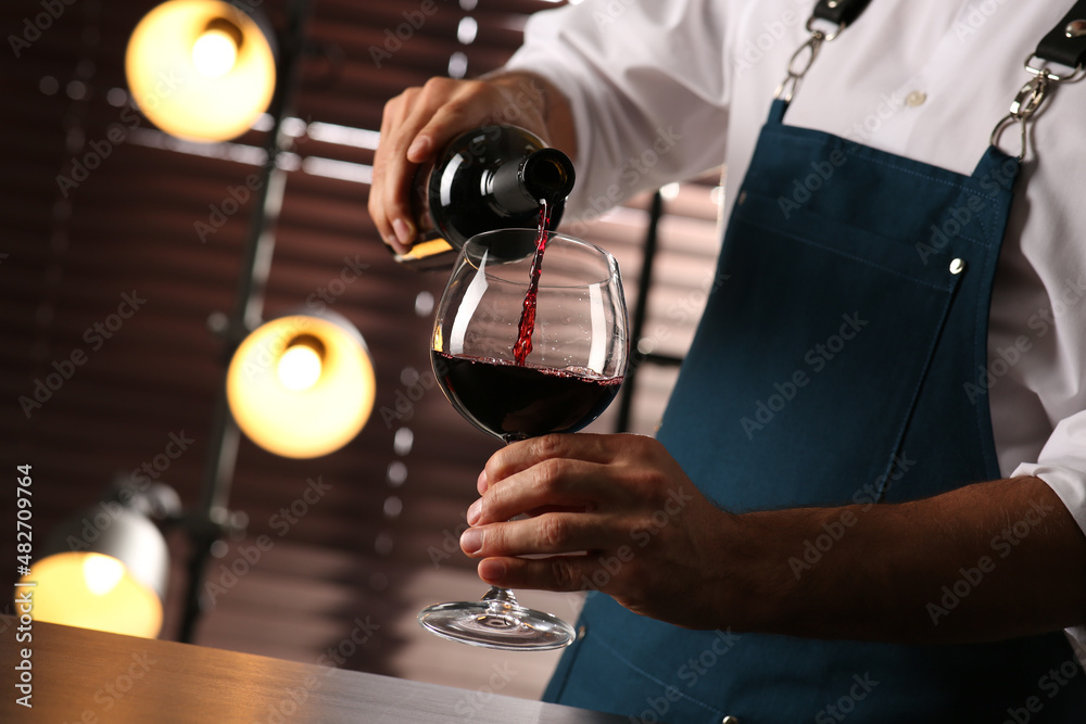 Bartender pouring red wine into glass indoors, closeup