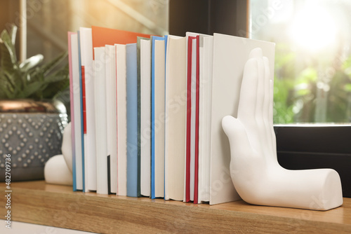 Beautiful hand shaped bookends with books on window sill indoors photo