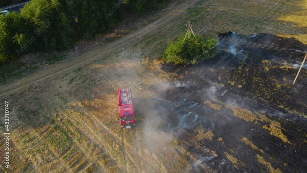 Aerial view rapid response firefighters brigade with fire truck on burning field of dry stubble. Emergency case for danger mission and rescue nature saving concept Aerial view rapid response firefighters brigade with fire truck on burning field of dry stubble. Emergency case for danger mission and rescue nature saving concept