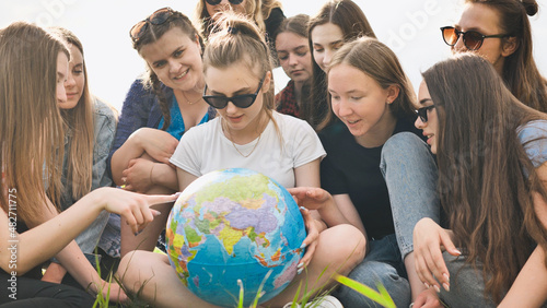 A group of cheerful girls is exploring the globe of the world in the meadow.