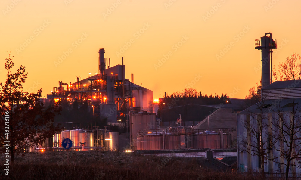 Factory surround with tanks and chimneys at sunset.