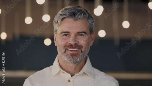 Successful aged man in formal outfit turning head and looking at camera while standing at the office building. Bearded caucasian person posing at office center.