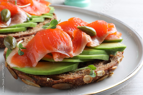 Delicious sandwich with salmon, avocado and capers on plate, closeup
