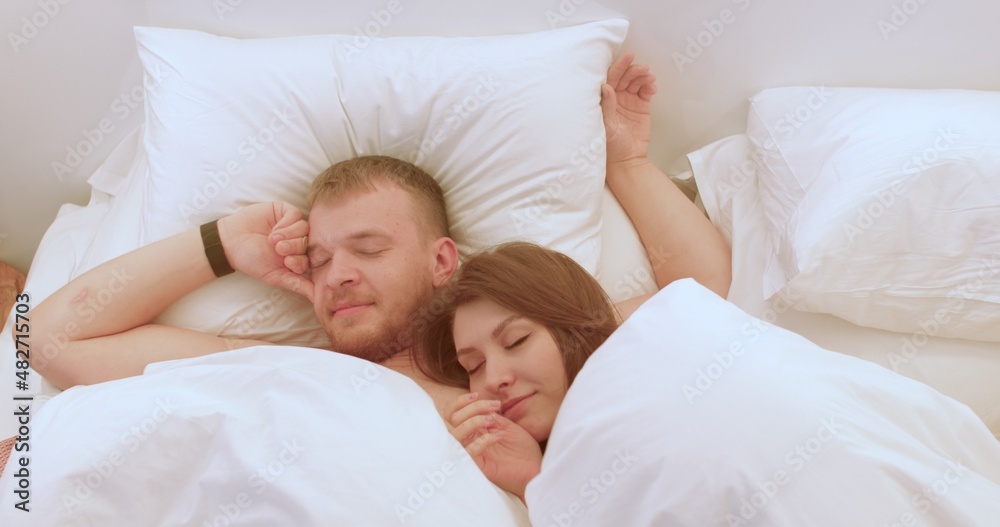 Sweet awakening of the newlyweds after their wedding night. Young man and woman communicate affectionately. White linen on the bed in the hotel. Sweet awakening of the newlyweds after their wedding night. Young man and woman communicate affectionately. White linen on the bed in the hotel.