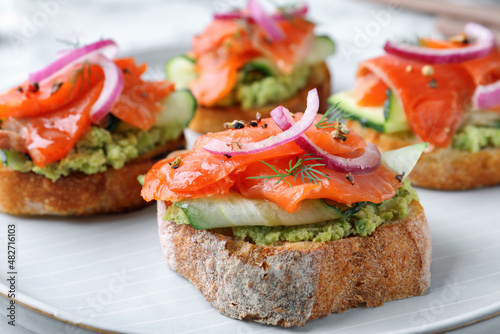 Delicious sandwiches with salmon, avocado, cucumber and onion on plate, closeup