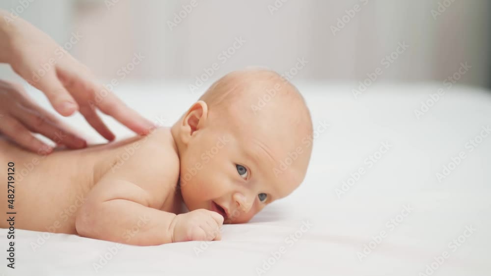 the baby lies on his tummy on a white sheet. and mom's hands massage the back. the baby lies on his tummy on a white sheet. and mom's hands massage the back.