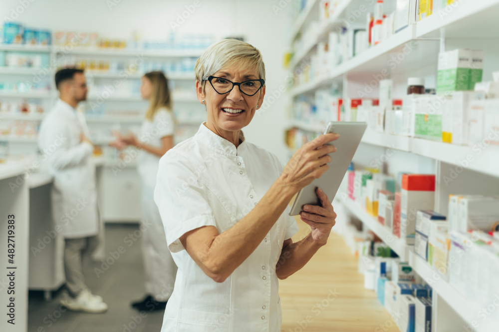 Beautiful senior female pharmacist checking medications on a shelf
