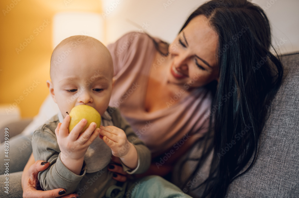 Mother playing with baby boy and eating a healthy food Mother playing with baby boy and eating a healthy food
