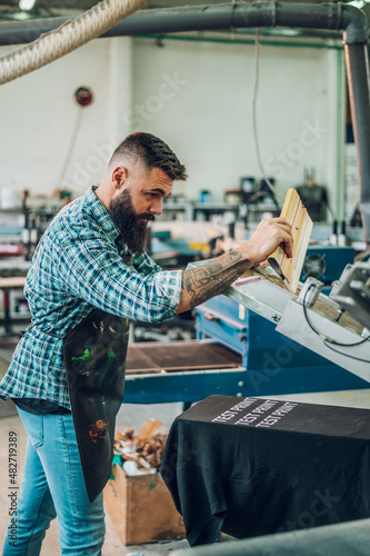 Worker pressing ink on frame while using the printing machine in a workshop