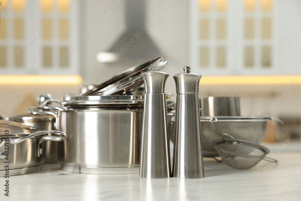 Set of shiny cooking utensils on white table against blurred background Set of shiny cooking utensils on white table against blurred background