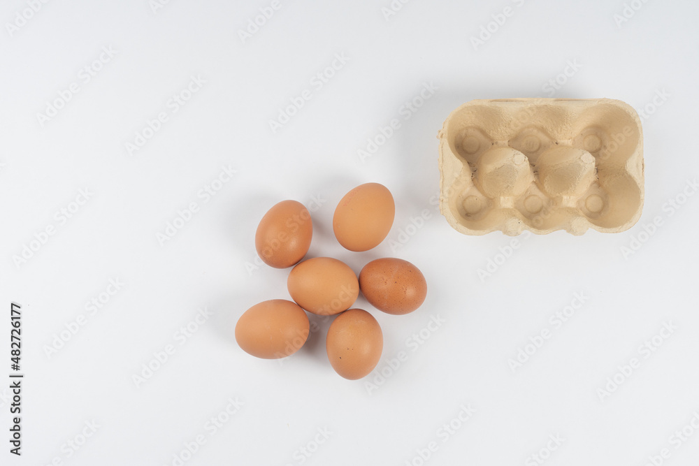 chicken brown eggs lie and next to a box for transportation, on a white background There is a place for text. chicken brown eggs lie and next to a box for transportation, on a white background There is a place for text.