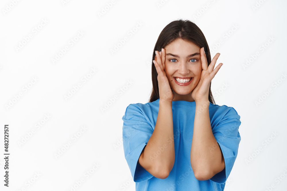 Portrait of smiling young woman looking amazed and excited, pleased by smth, standing in tshirt over white background Portrait of smiling young woman looking amazed and excited, pleased by smth, standing in tshirt over white background