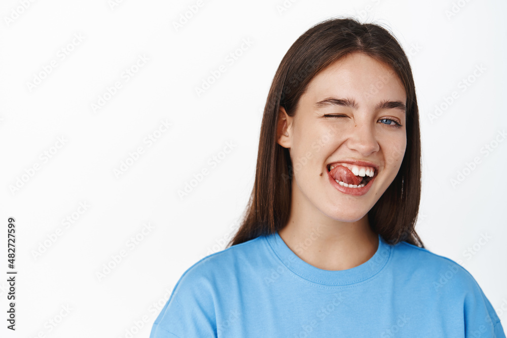 Close up portrait of smiling beautiful girl student, showing tongue, healthy teeth, winking happy at camera, white background Close up portrait of smiling beautiful girl student, showing tongue, healthy teeth, winking happy at camera, white background