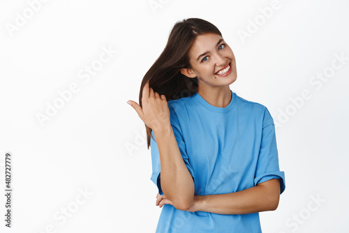 Beautiful healthy girl with long dark glowing hair and perfect facial skin, smiling happy at camera, wearing blue tshirt, white background © Cookie Studio