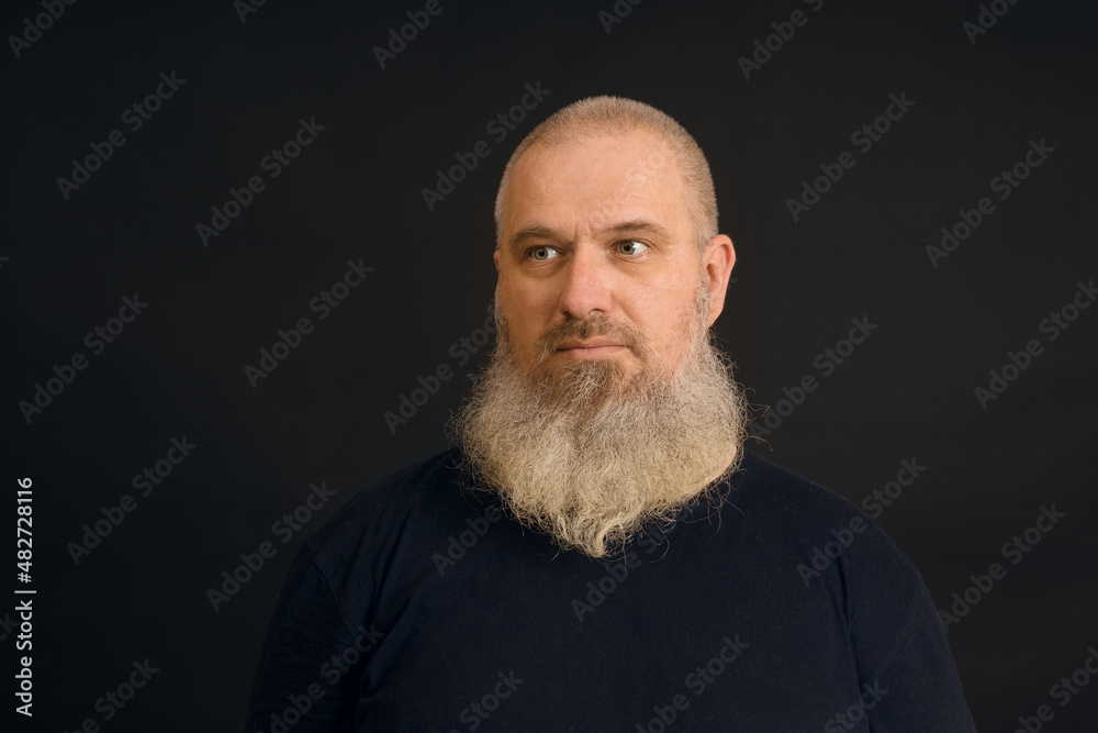 Obraz premium a man with an unshaven gray beard looks to the side on a black background, close-up