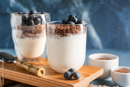 Glasses of sweet yogurt, flax seeds and blueberries on color background, closeup