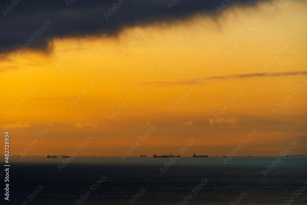 silhouettes of ships at sea, dramatic seascape with sunset sky, sunlight reflected from the waves