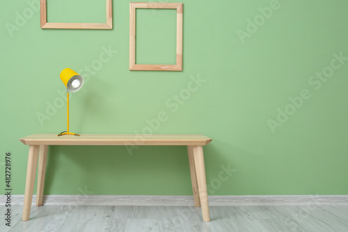 Glowing lamp on table and empty wooden frames on color wall