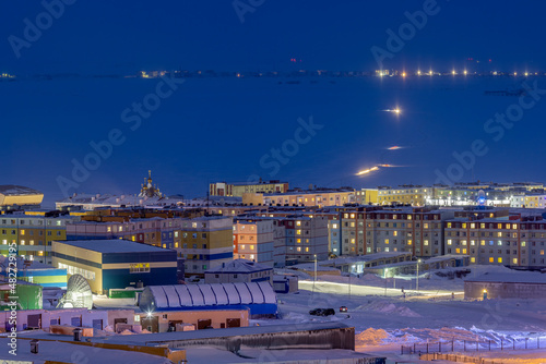 Night view from above on a snow-covered northern city in the Arctic. In the distance is an ice crossing across the frozen Anadyr estuary. Cold winter weather. Anadyr  Chukotka  Far North of Russia.