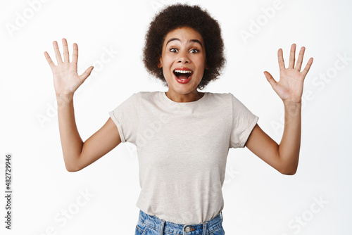 Excitement. Enthusiastic black girl looking amazed and fascinated, checking out big awesome news, raising hands up and gasping in awe, standing over white background