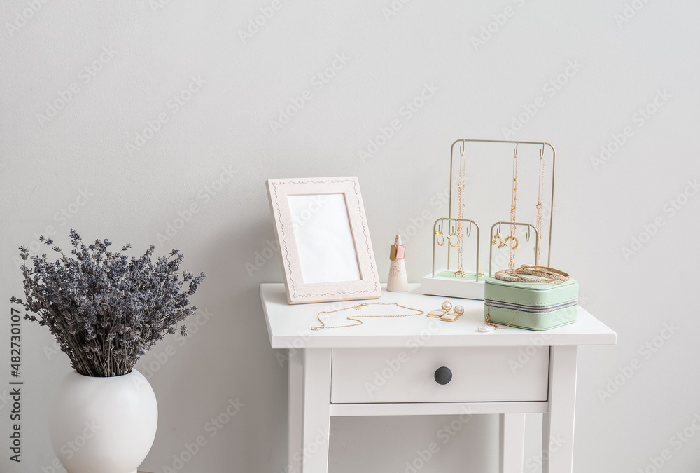 Fototapeta premium Table with stylish jewelry and vase with flowers near light wall