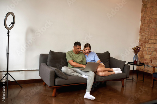 Multiracial blogger couple using laptop at home