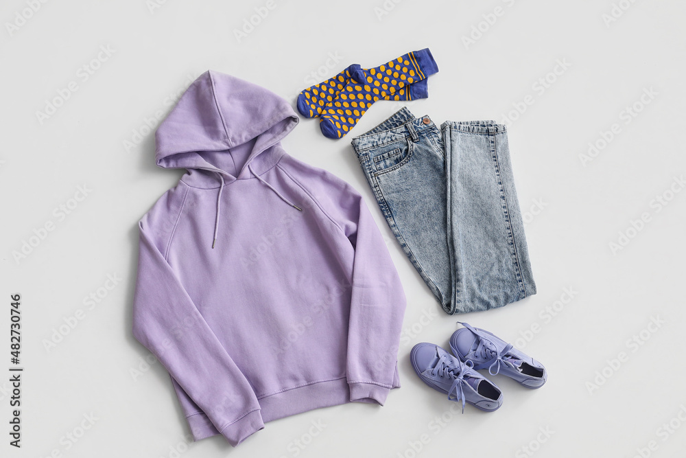 Stylish lilac hoodie with socks, jeans and sneakers on light background