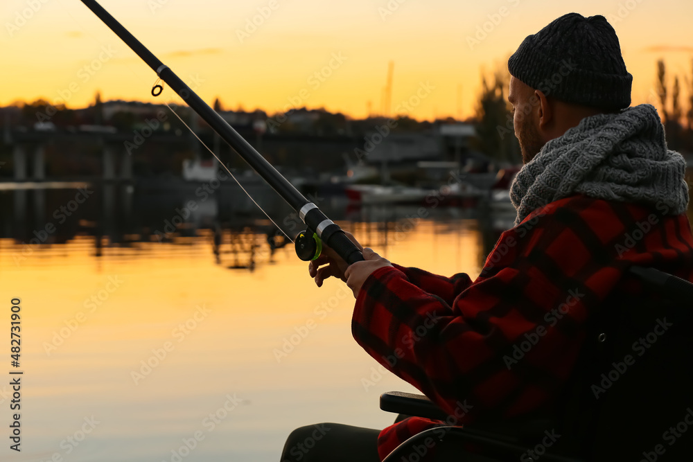 Fototapeta premium Man in wheelchair fishing on river at sunset